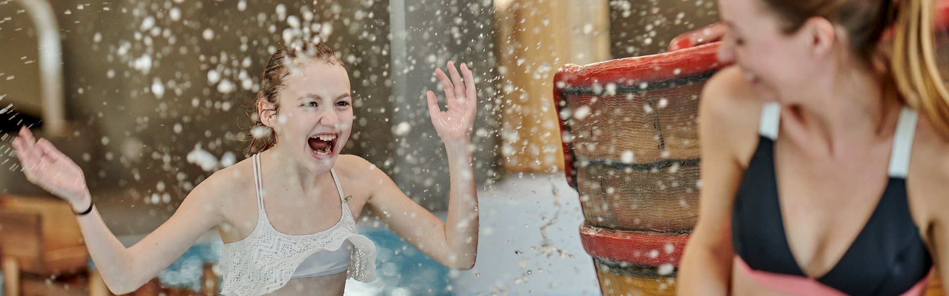 Eine Frau und ein Mädchen lachen und stehen im Indoor-Pool