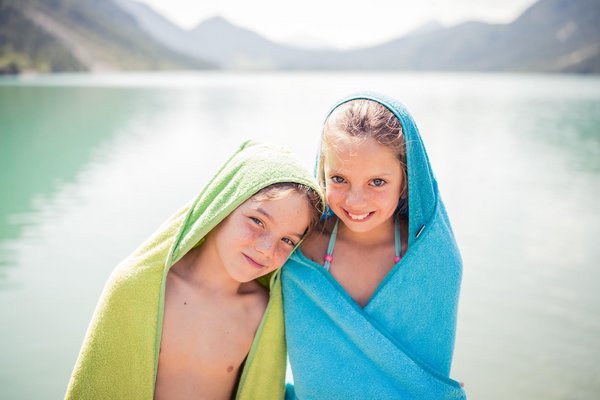 Zwei Kinder mit Handtuch stehen am See-Strand 