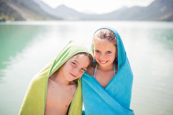 Zwei Kinder mit Handtuch stehen am See-Strand 