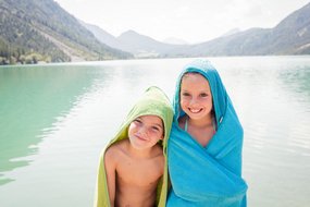 Zwei Kinder stehen am See mit einem Handtuch
