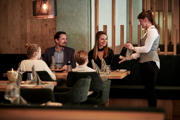 Familie am Esstisch bekommt einen Wein serviert