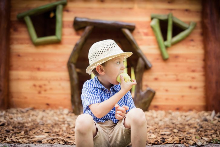 Kind isst einen Apfel vor dem Kinderspiel-Haus 