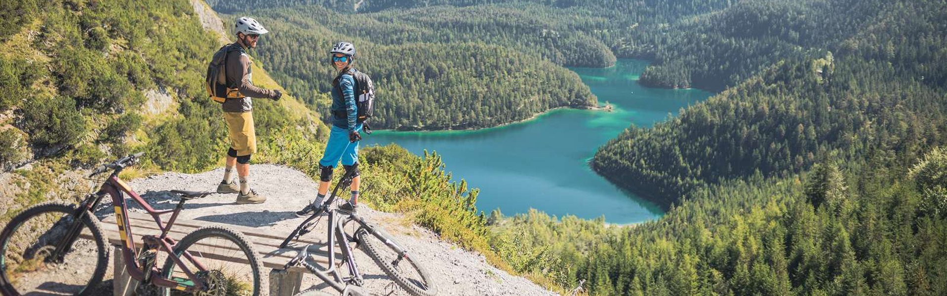 Paar steht auf Anhöhe und genießt das herrliche Panorama und den Blick auf einen Bergsee