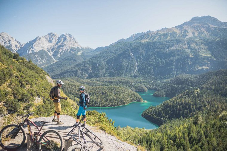 Paar steht auf Anhöhe und genießt das herrliche Panorama und den Blick auf einen Bergsee