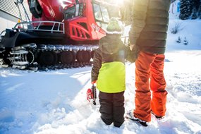 Kleiner Bub steht mit Vater vor einer Pistenraube im Schnee