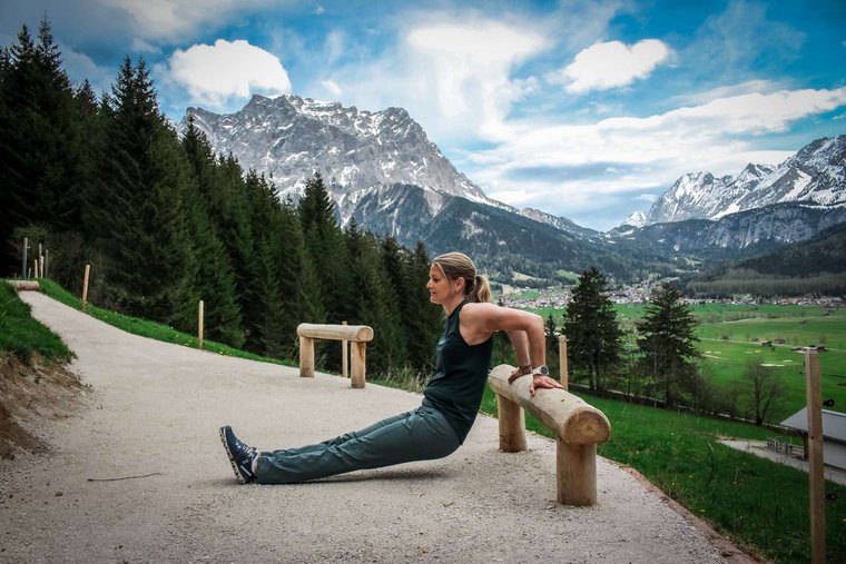 Frau macht Sportübung vor Berglandschaft auf einem Outdoor-Fitnessgerät